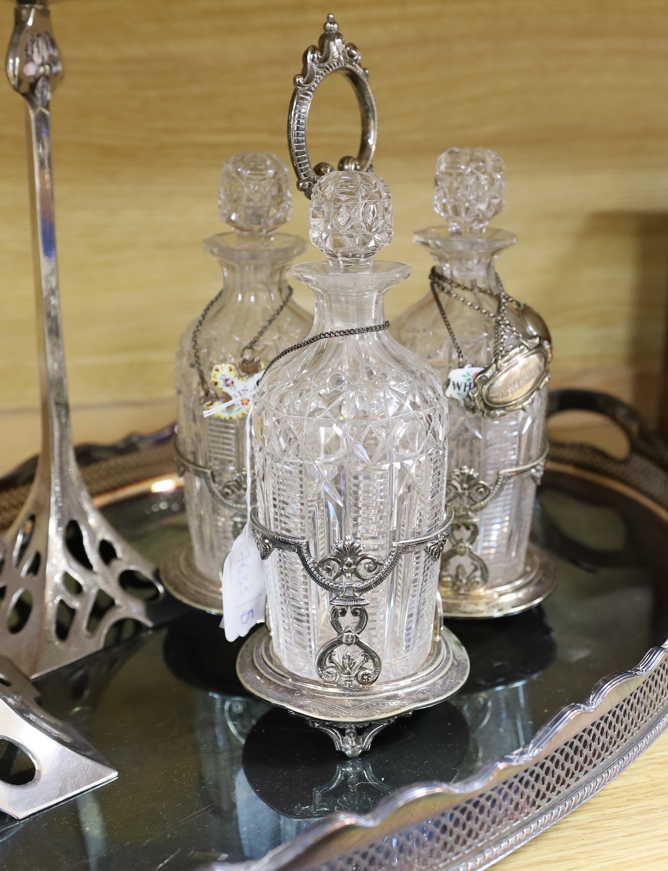 An oval silver plated tray, a three bottled tantalus and a pair of candlesticks, a silver ‘Whiskey’ label, two enamelled silver labels ‘Gin’ and ‘Whisky’ and two plated labels